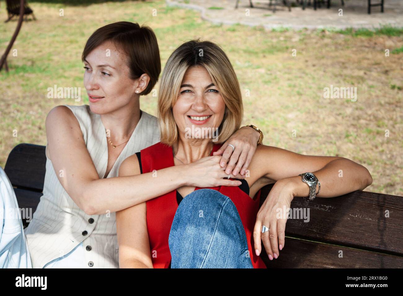 two fashionable women sitting on a wooden bench, outdoors Stock Photo
