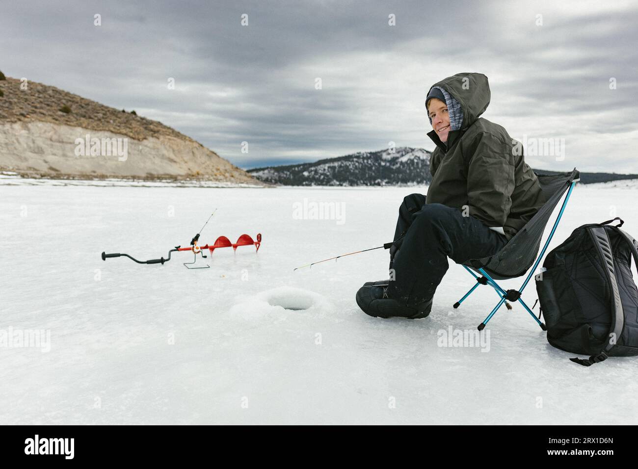 Frozen lake with a boy ice fishing in hole in snow in winter Stock Photo