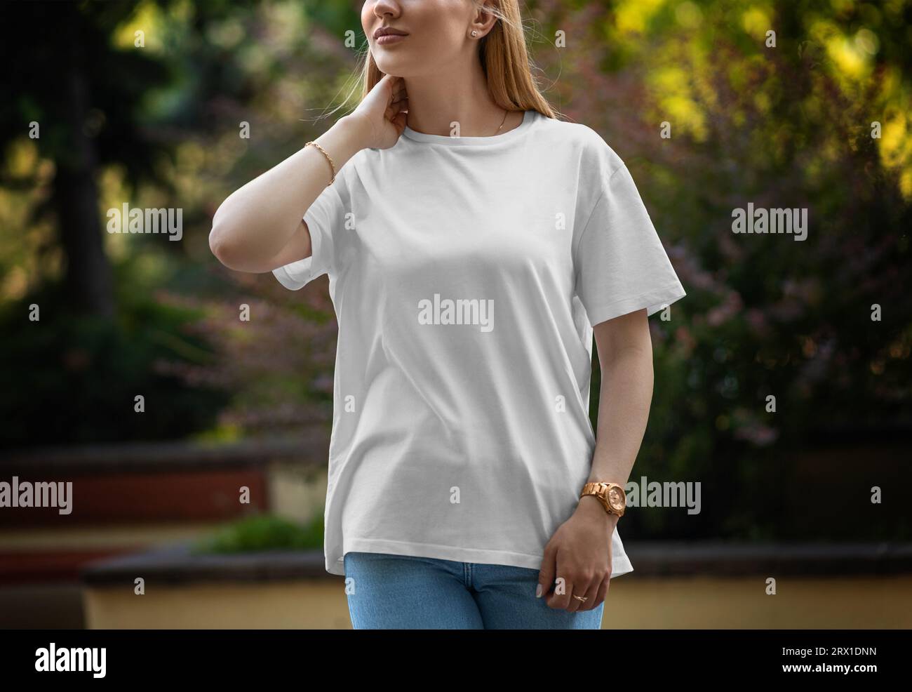Mockup of a white stylish t-shirt on a posing girl on a blurred background of a green park, front view. Streetwear template for presentation of design Stock Photo
