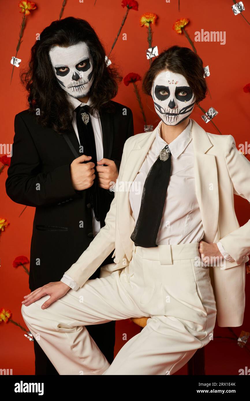 elegant couple in catrina makeup and suits posing on red background