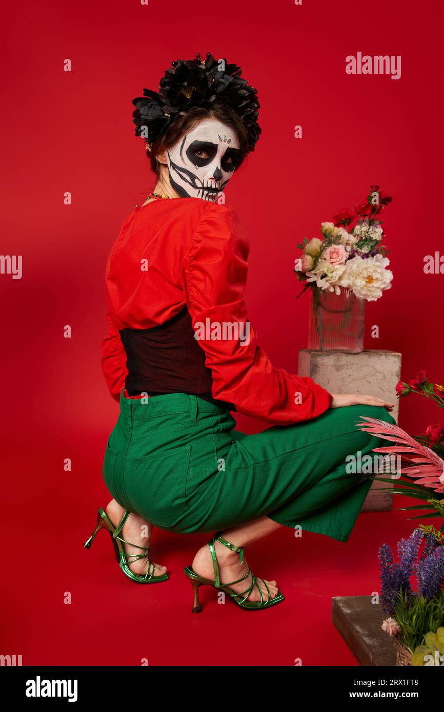 woman in dia de los muertos makeup looking at camera near traditional