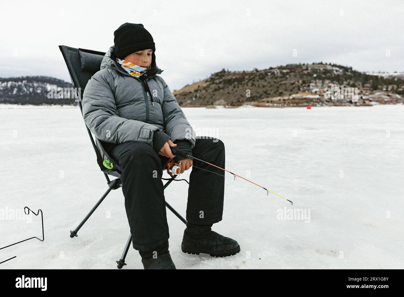 Teenage boy using fishing pole on frozen lake in winter Stock Photo