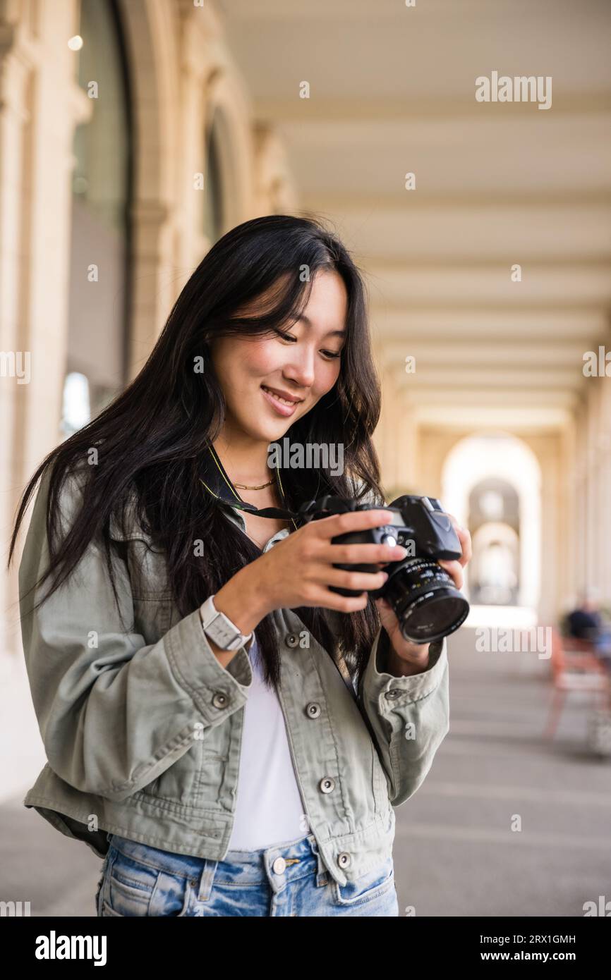 Smiling young female photographer looking at her camera in the street. Stock Photo