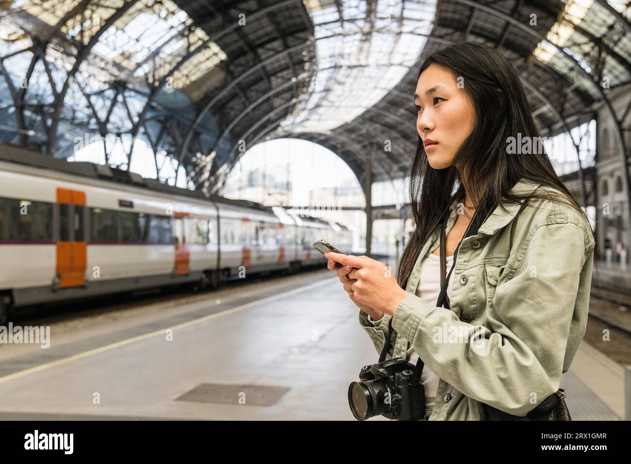 Young female traveler checking her phone in train station. Stock Photo