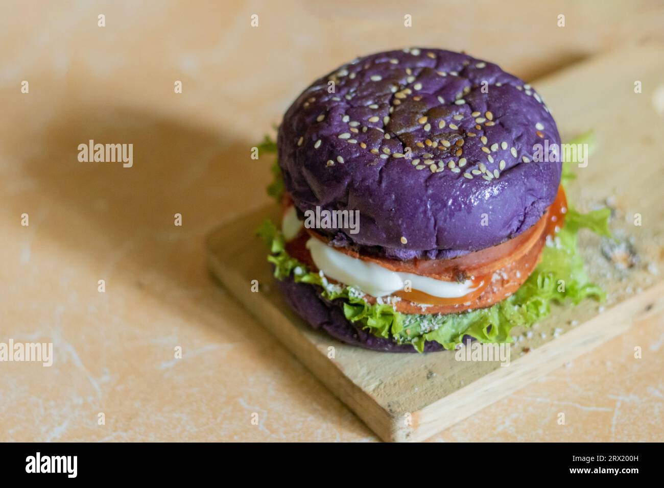 close up photo of a home-made purple burger placed on a ceramic table. Hamburger. Fast Food. Culinary Stock Photo