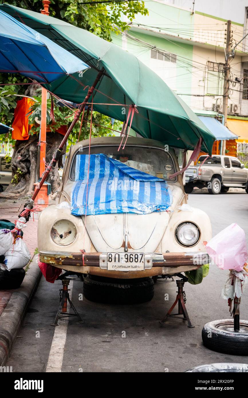 A very old ruined Volkswagen Beetle car sits under some umbrellas in the China Town area of Bangkok, Thailand. Stock Photo