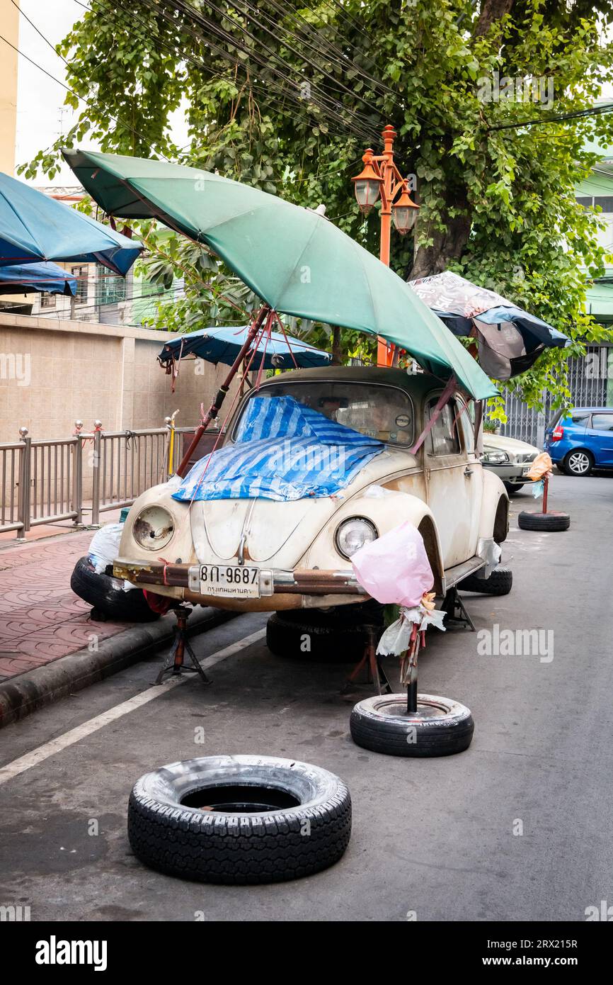 A very old ruined Volkswagen Beetle car sits under some umbrellas in the China Town area of Bangkok, Thailand. Stock Photo