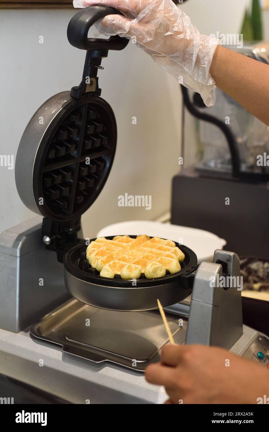 the cook check the dough for sweet waffles into the waffle iron with a wooden stick Stock Photo