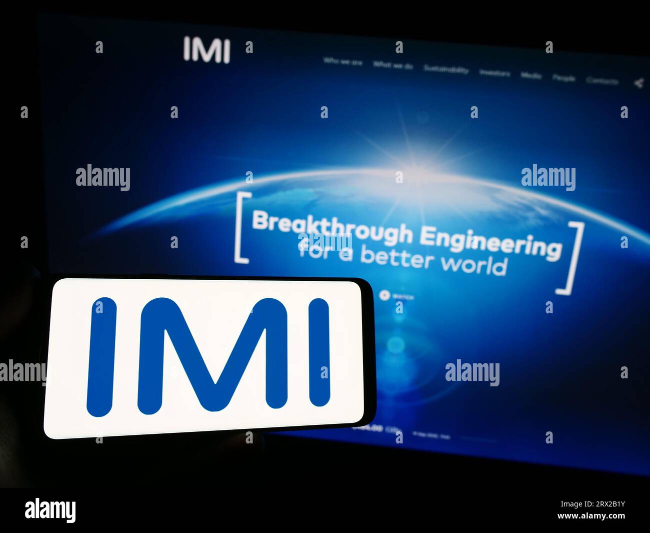 Person holding smartphone with logo of British engineering company IMI plc on screen in front of website. Focus on phone display. Stock Photo