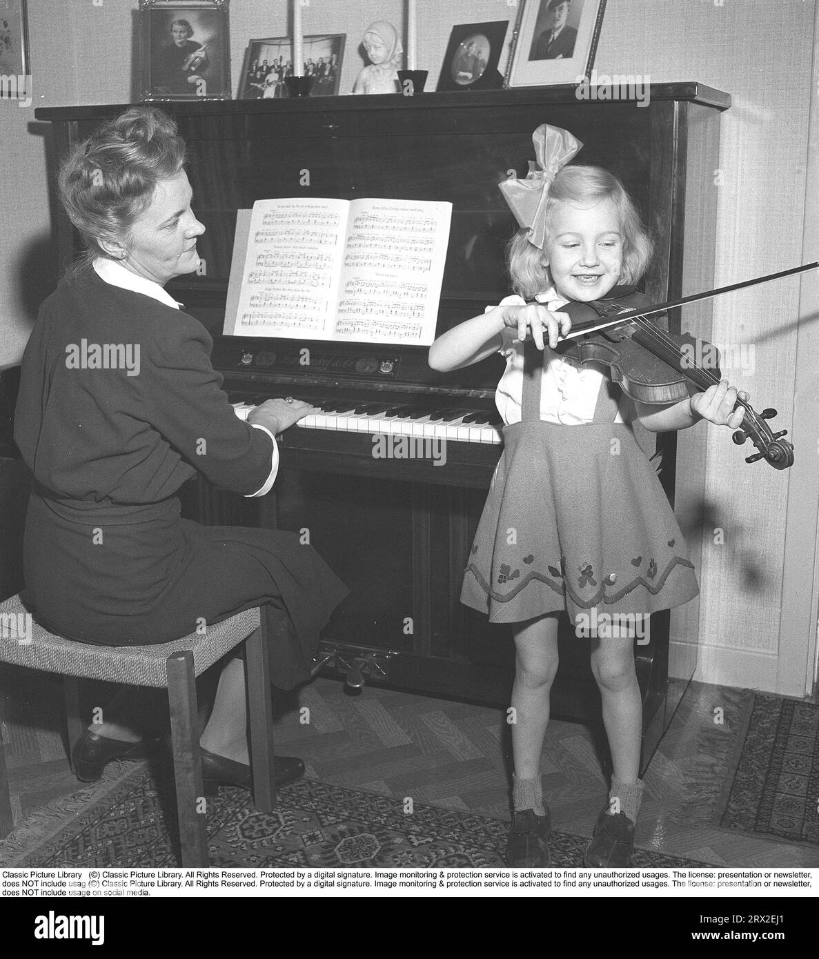 In the 1940s. A mother and her daughter play music together at home. Mother plays the piano and daughter plays the violin. The sheet music contains, among other things, the melody Come little girl waltz with me. Sweden 1946. Kristoffersson ref Y98-3 Stock Photo