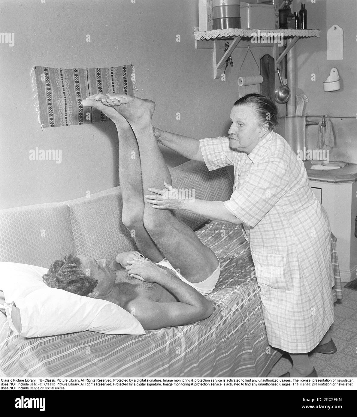 Massage in the 1950s. An old woman gives a younger man, who is lying on a bed, treatment in the form of massage and stretching. Sweden 1954. Kristoffersson ref BM9-3 Stock Photo