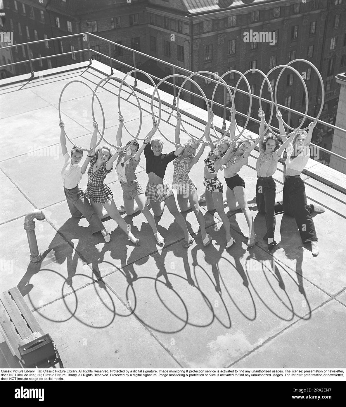 Gymnastics in the 1940s. Young female gymnasts are standing on a rooftop in Stockholm city forming a symmetrical image with the rings shadows in front of them when holding the rings above themselves and posing as they do. Sweden 1945 Kristoffersson ref O143-1 Stock Photo