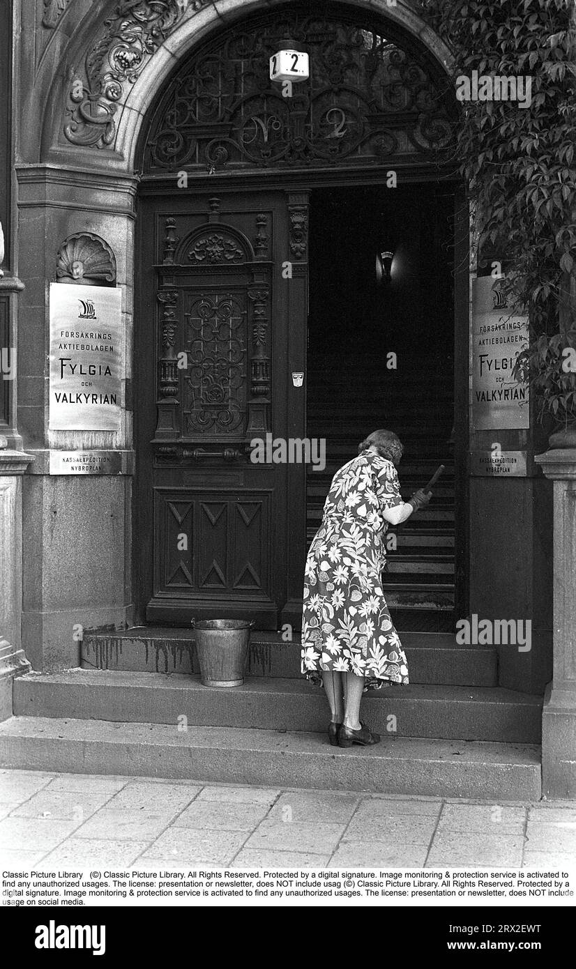 Ordinary people at work in the 1950s. An elderly cleaning lady is seen cleaning the steps of the entrance to a building.  Sweden 1953 Kristoffersson ref Fold1 Stock Photo
