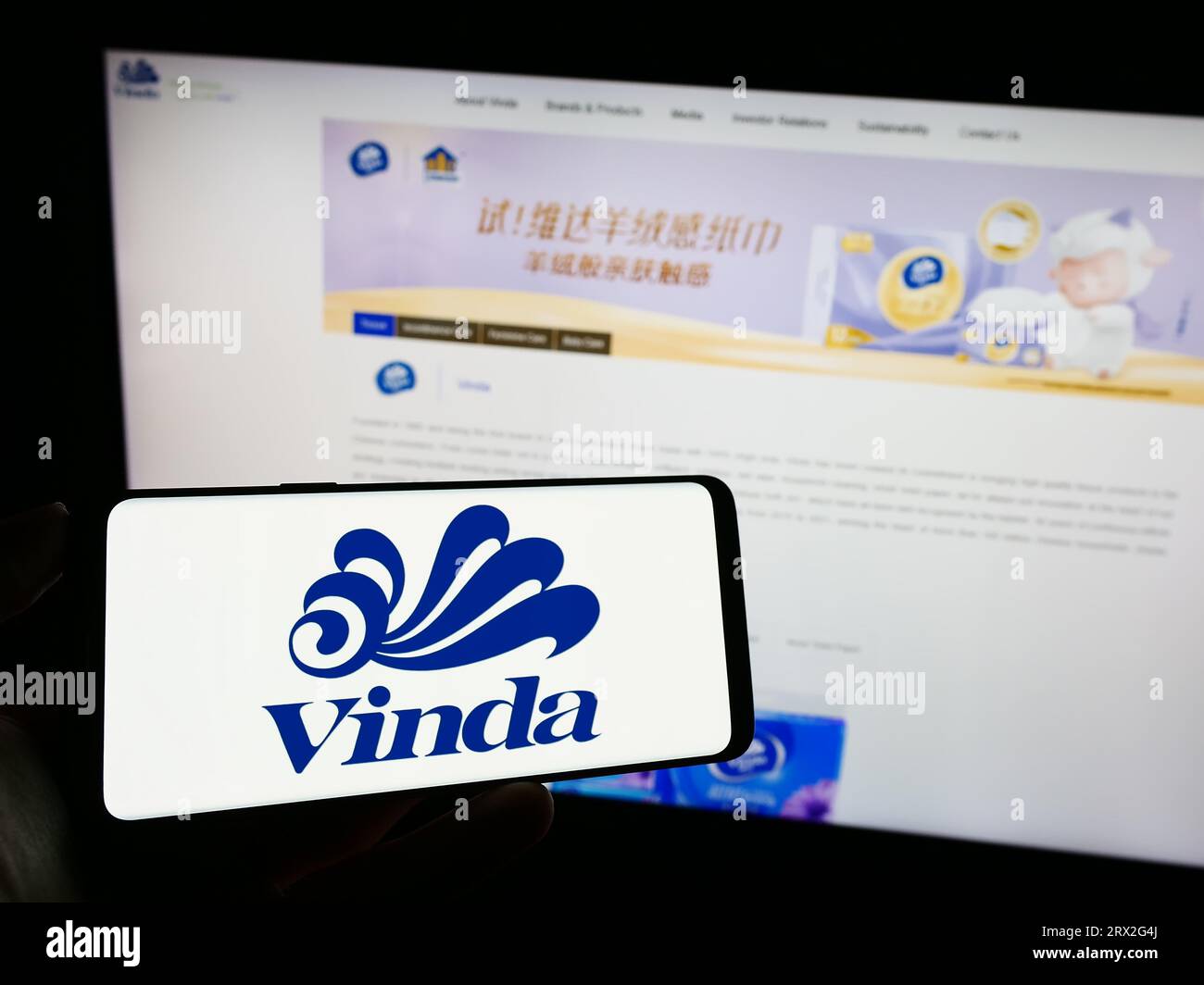 Person holding mobile phone with logo of company Vinda International Holdings Limited on screen in front of web page. Focus on phone display. Stock Photo