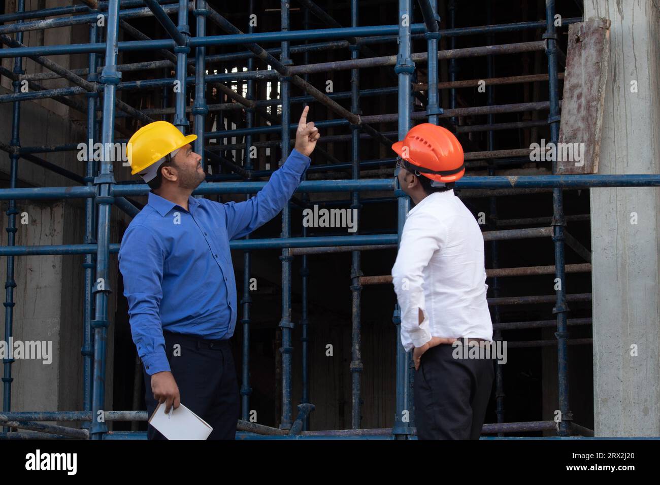Two architect wearing safety helmet talking about construction project and pointing finger up at site. Repair, construction and maintenance concept Stock Photo