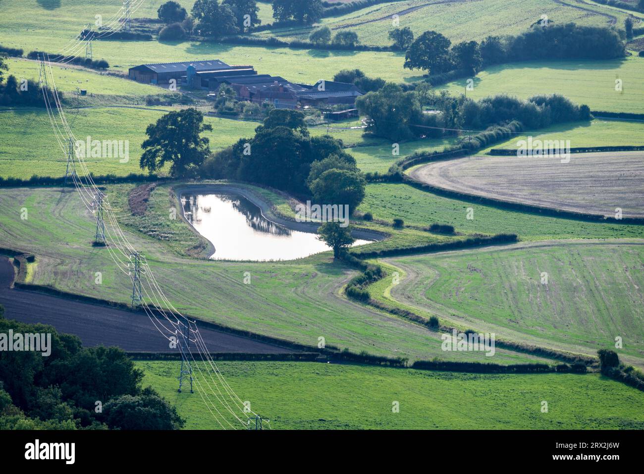 High voltage electricity cables,hanging from steel pylons,passing westwards,over green fields and agricultural farmland of scenic rural England,reflec Stock Photo