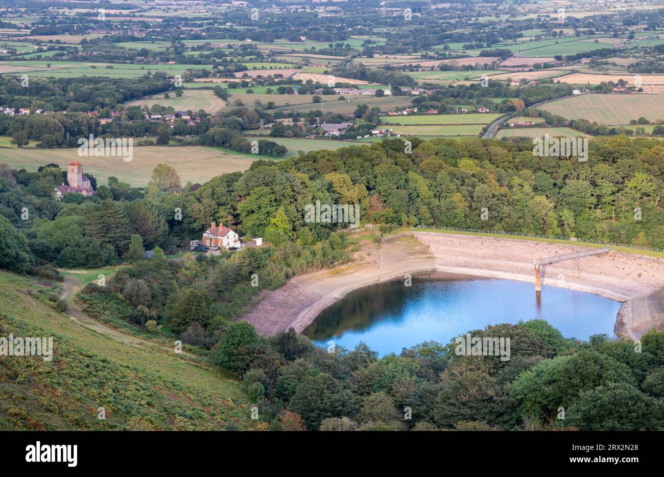 View fron the summit of the ancient,historic Iron Age hill fort,a Scheduled Ancient Monument hill.Resevoir pond surrounded by lush,green woodland tree Stock Photo