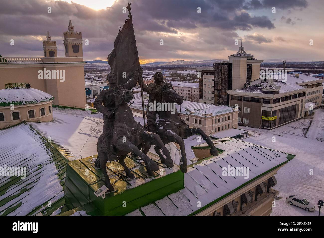 The old Soviet bronze statue of the Buryat horsemen with the flag on the top of the Ulan-Ude theater in Buryatiya, Russia, during the winter sunset. Stock Photo