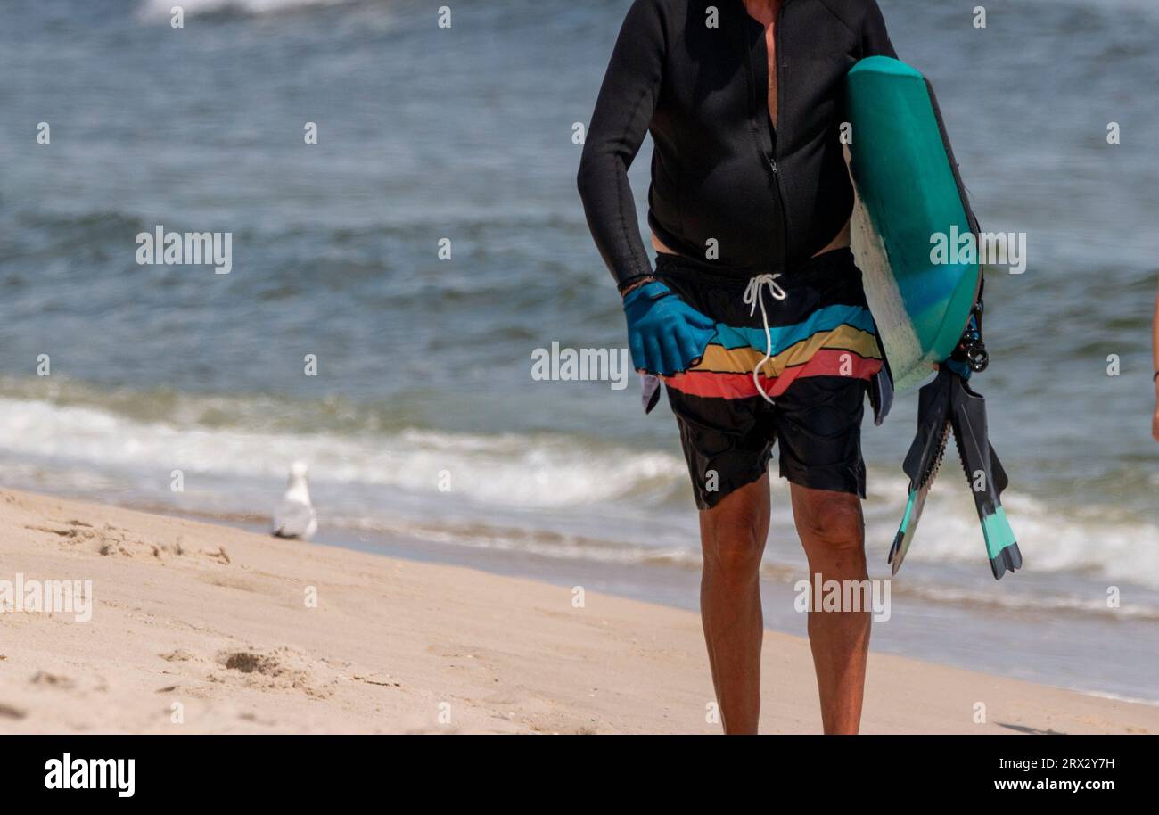 Man walking on the beach carrying a boogie board under his arms and flippers in his hands. Stock Photo