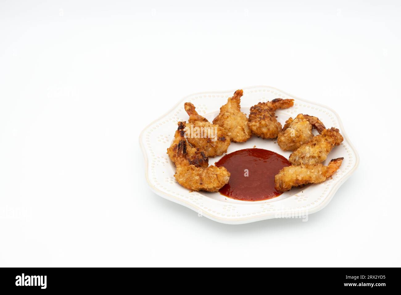 Tasty baked coconut shrimp with red cocktail sauce.  Tail-on, jumbo shrimp coated in a coconut breadcrumb topping and served with red cocktail sauce Stock Photo