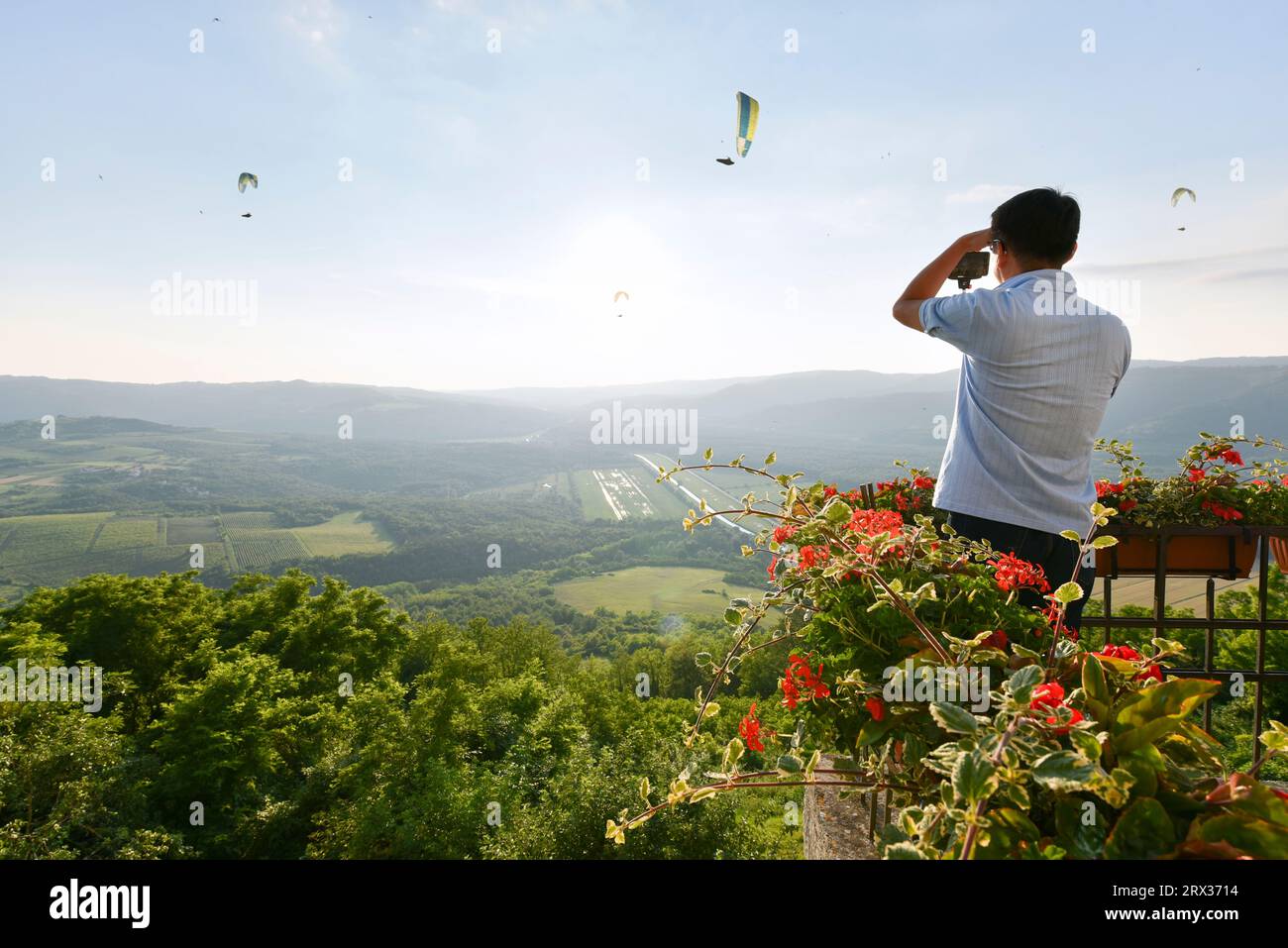 A tourist photographs paragliders from atop the hilltop village of Motovun, Istria, Croatia, Europe Stock Photo