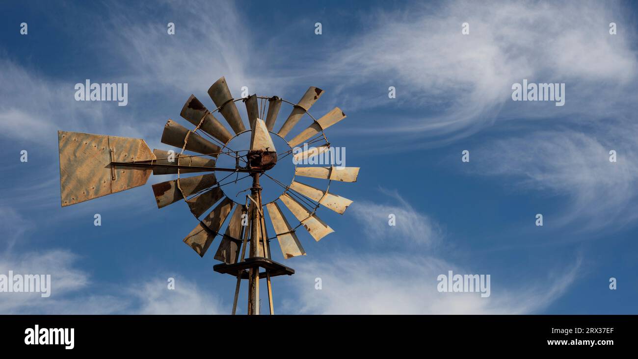 old-fashioned, multi-bladed, metal wind pump atop a tower against a blue sky. Stock Photo