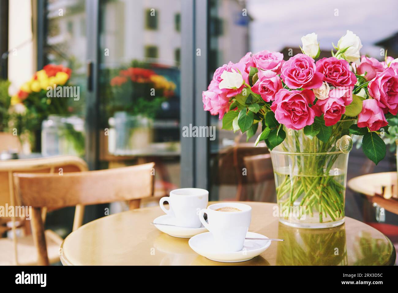 Vase with pink flowers and two cups of coffee in outdoor cafe, love and romance concept Stock Photo