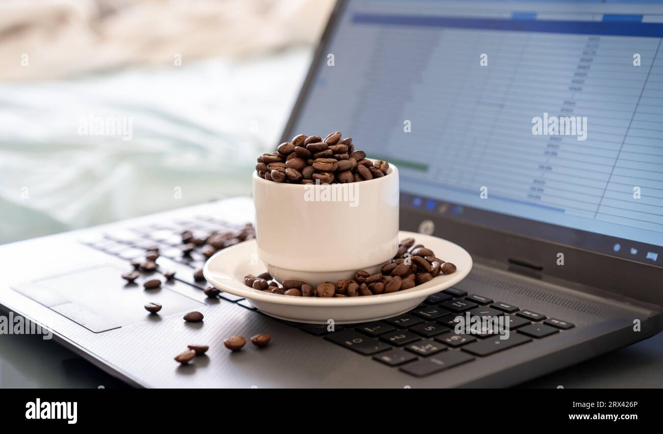 Cup of coffee that full of coffee beans on laptop background with rim light represents working while drinking coffee Stock Photo