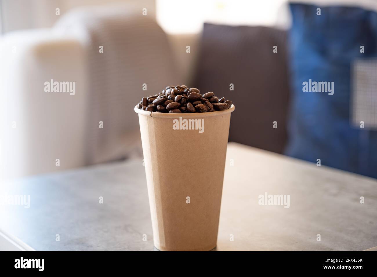 paper cup of coffee full of coffee beans  with couch background Stock Photo
