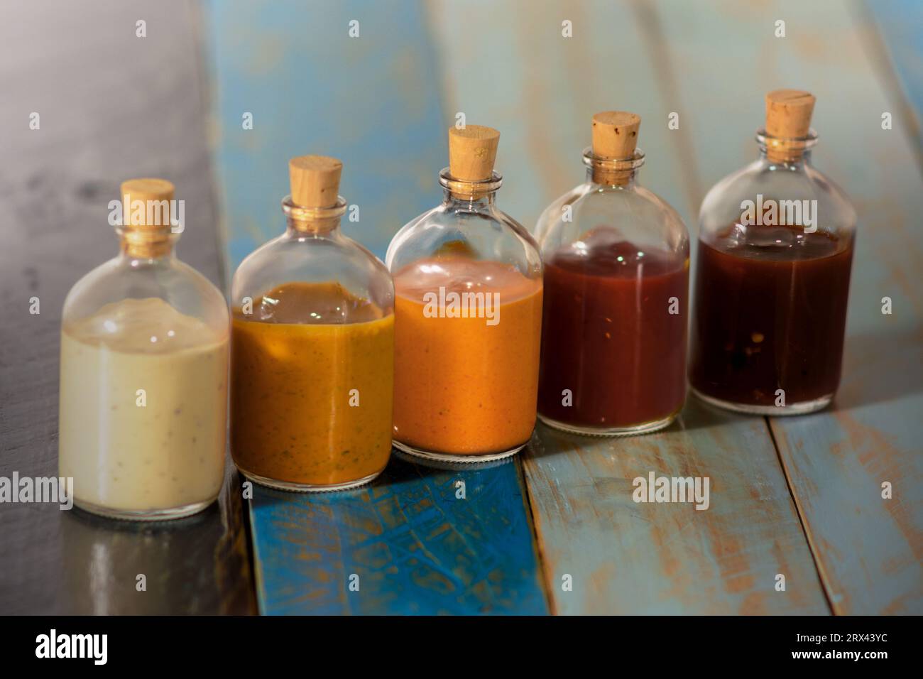 Handmade spicy sauces in glass bottles with cork on a colored wooden base - Salsas picantes hechas artesanalmente en botellas de vidrio con corcho sob Stock Photo