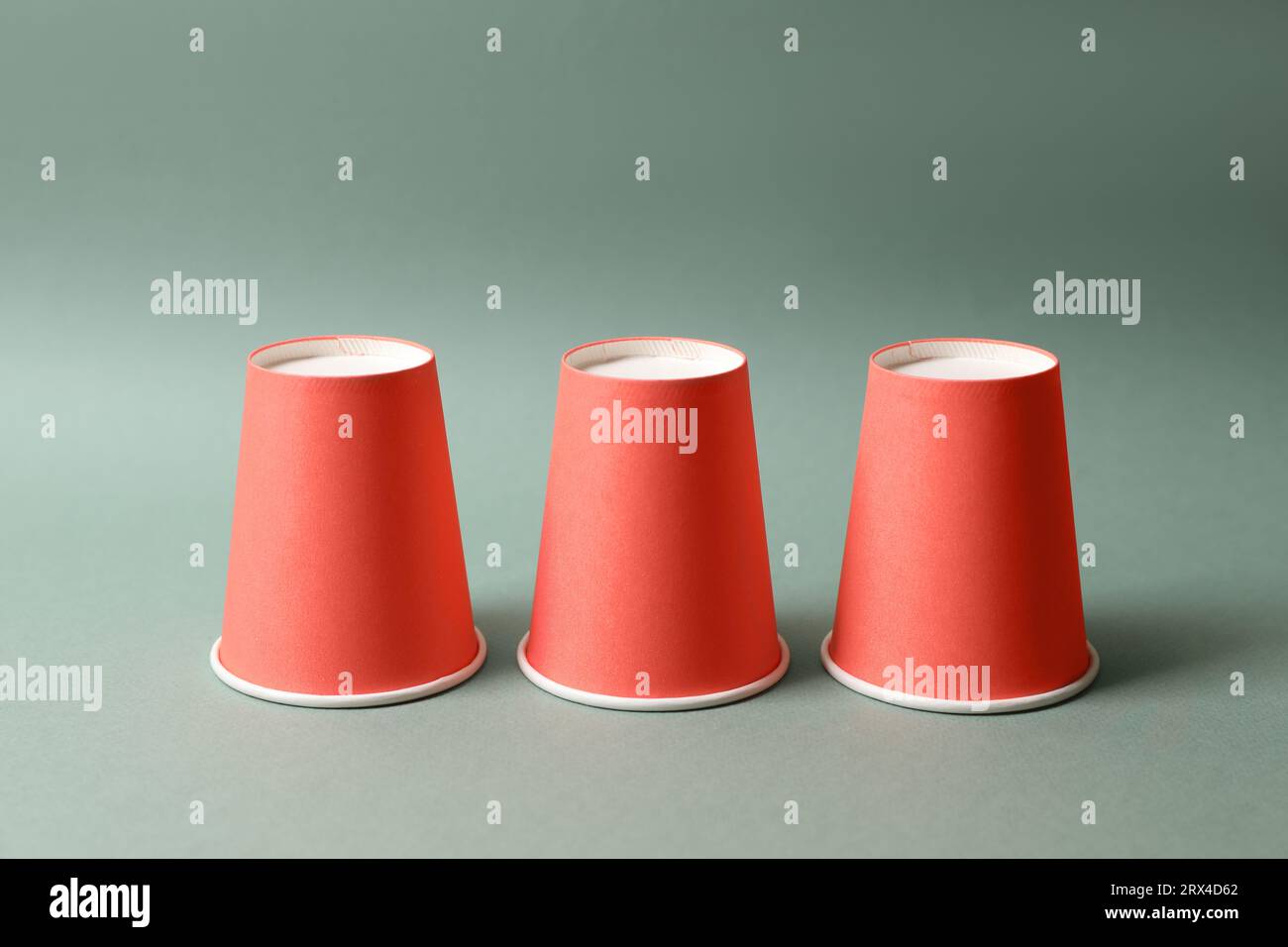 Three red cups on pale olive background. Thimblerig game Stock Photo ...