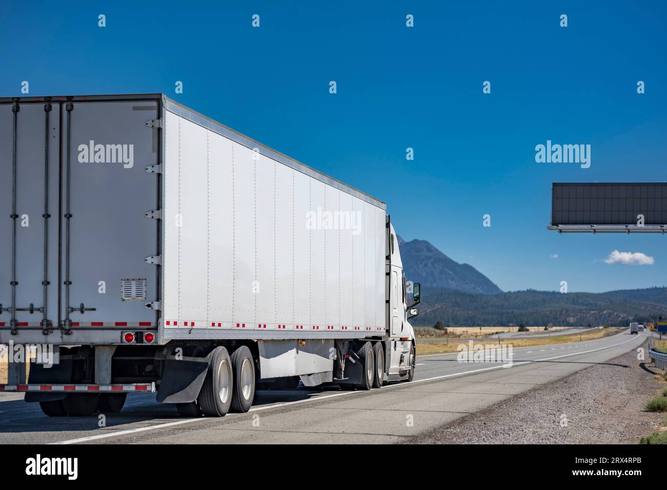 Industrial grade long hauler carrier white big rig semi truck tractor transporting commercial cargo in dry van semi trailer running on the straight di Stock Photo