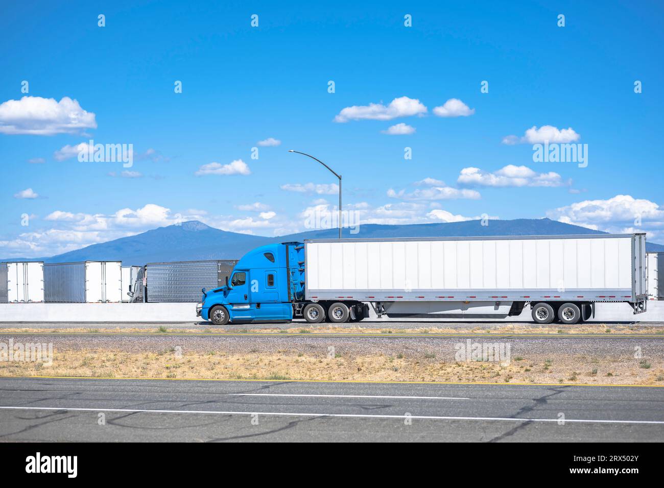 Industrial grade loaded long hauler carrier blue big rig semi truck tractor transporting commercial cargo in dry van semi trailer running on the highw Stock Photo