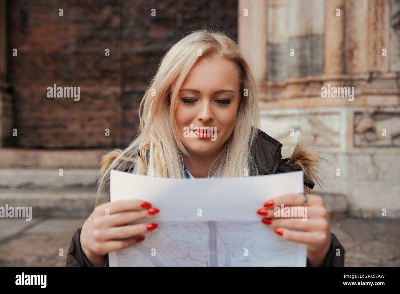 Holding a paper map, a young woman sports a self-ironic smile. She knows she'll soon rely on her smartphone's GPS, trading views of beautiful architec Stock Photo