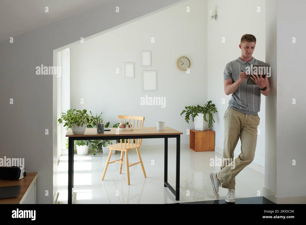 Young man leaning on wall when proofreading contract on tablet computer Stock Photo