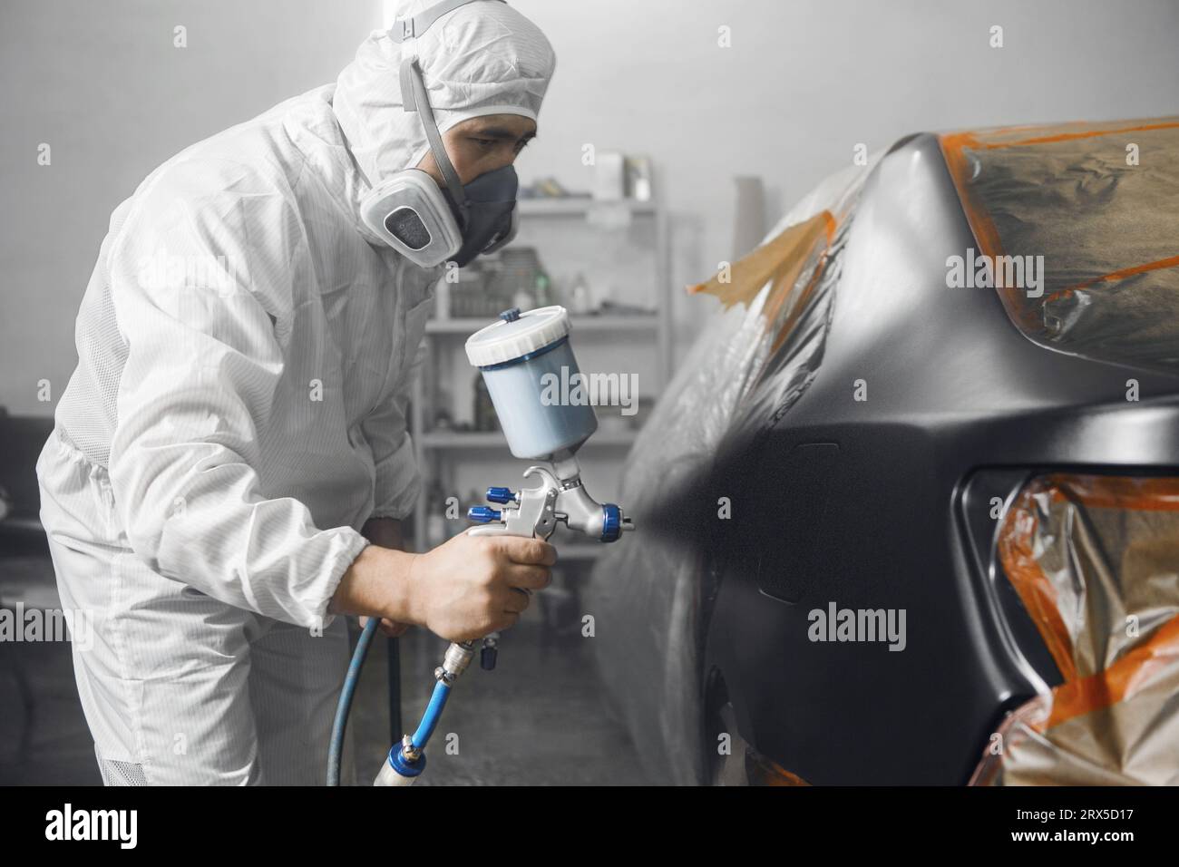 Body car painter with airgun spraying paint on part of automobile in