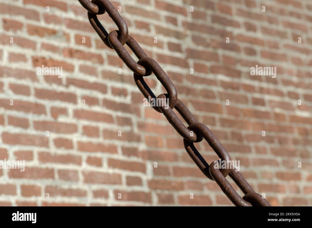 rusty chains brick background, a symbol of strength and oppression, used in industry in crowbars as well as for slavery. very large chain links. Stock Photo