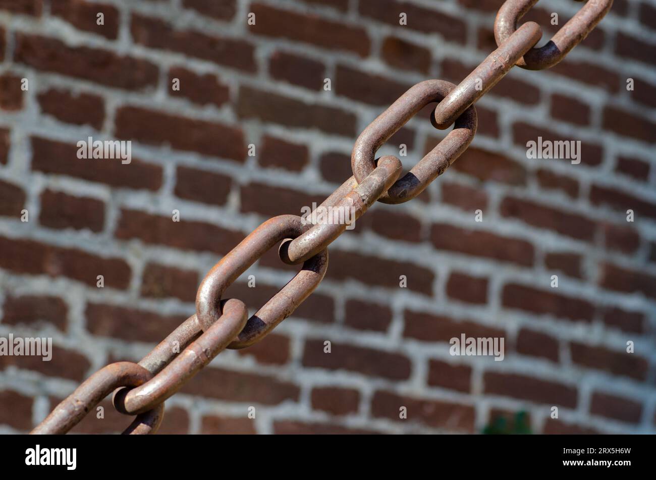rusty chains brick background, a symbol of strength and oppression, used in industry in crowbars as well as for slavery. very large chain links. Stock Photo