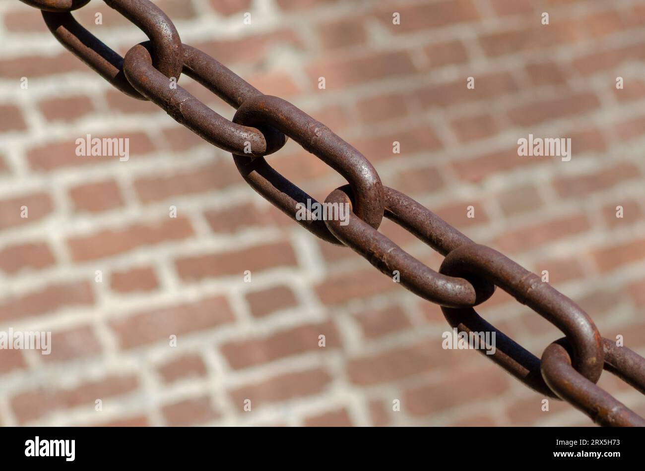 rusty chains brick background, a symbol of strength and oppression, used in industry in crowbars as well as for slavery. very large chain links. Stock Photo