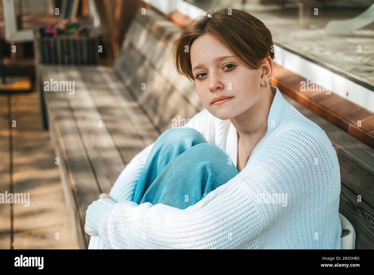 A teenage girl sits on a bench on the street, hugging her knees Stock ...