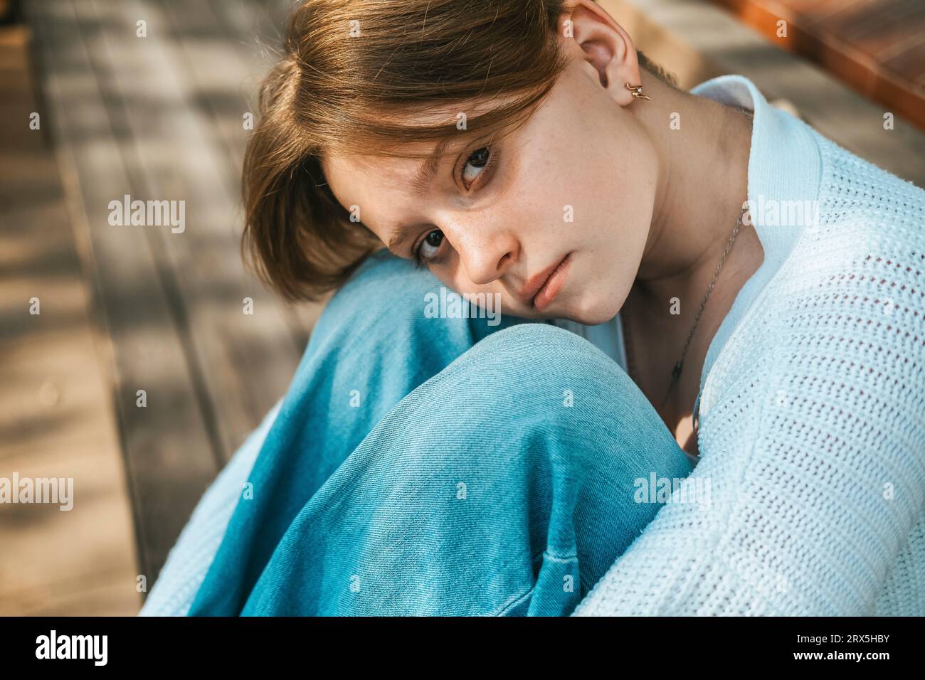 A teenage girl sits on a bench on the street, hugging her knees Stock ...