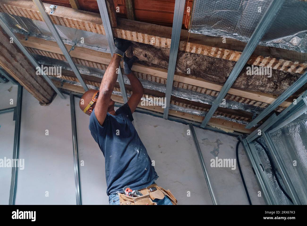 Construction worker installing insulation on ceiling in attic Stock