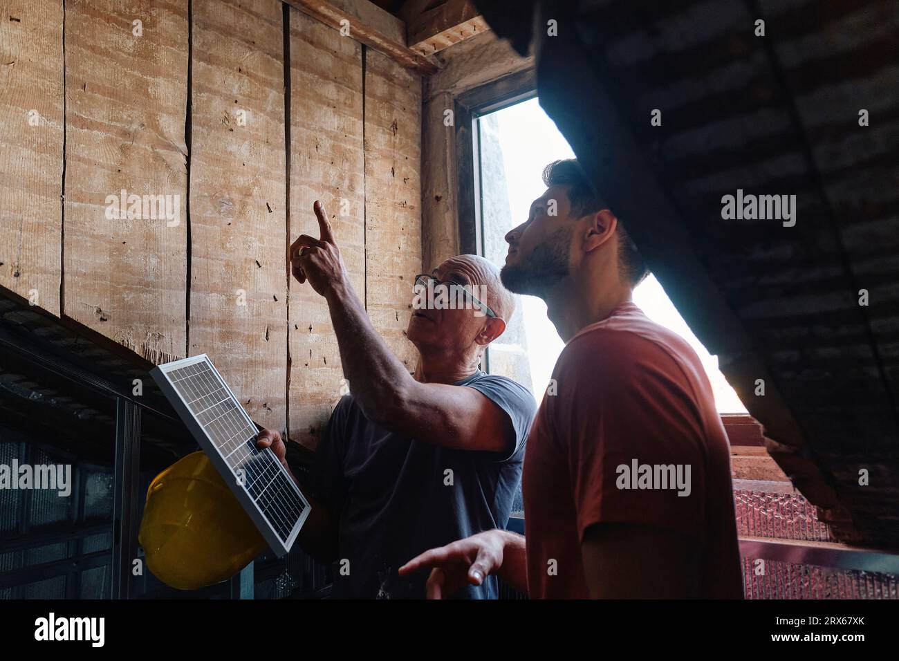 Construction worker holding solar panel and discussing with man at site Stock Photo