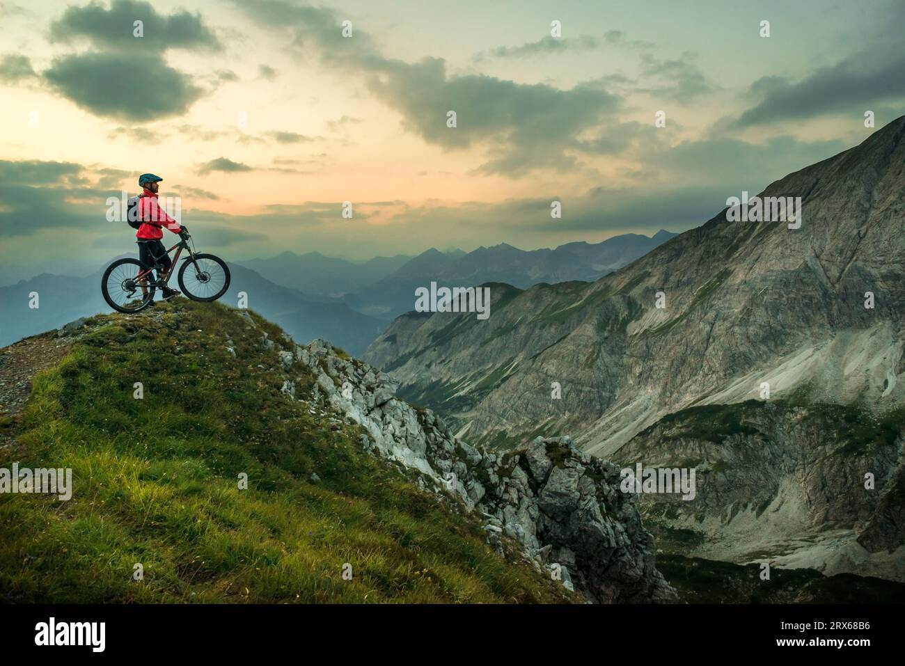Biker with bicycle on top of mountain under cloudy sky Stock Photo