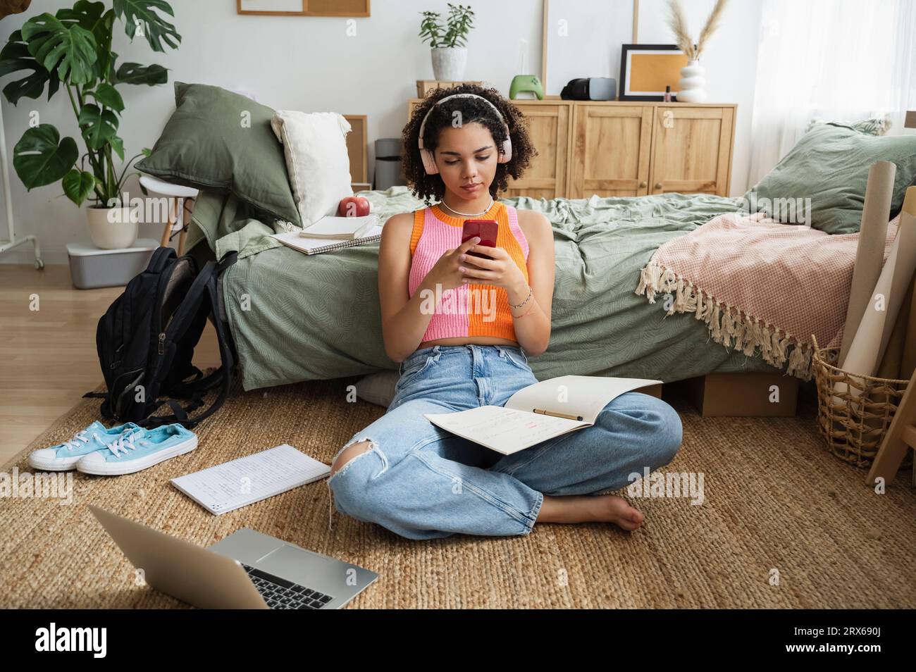 Teenage girl wearing wireless headphones using mobile phone on rug at