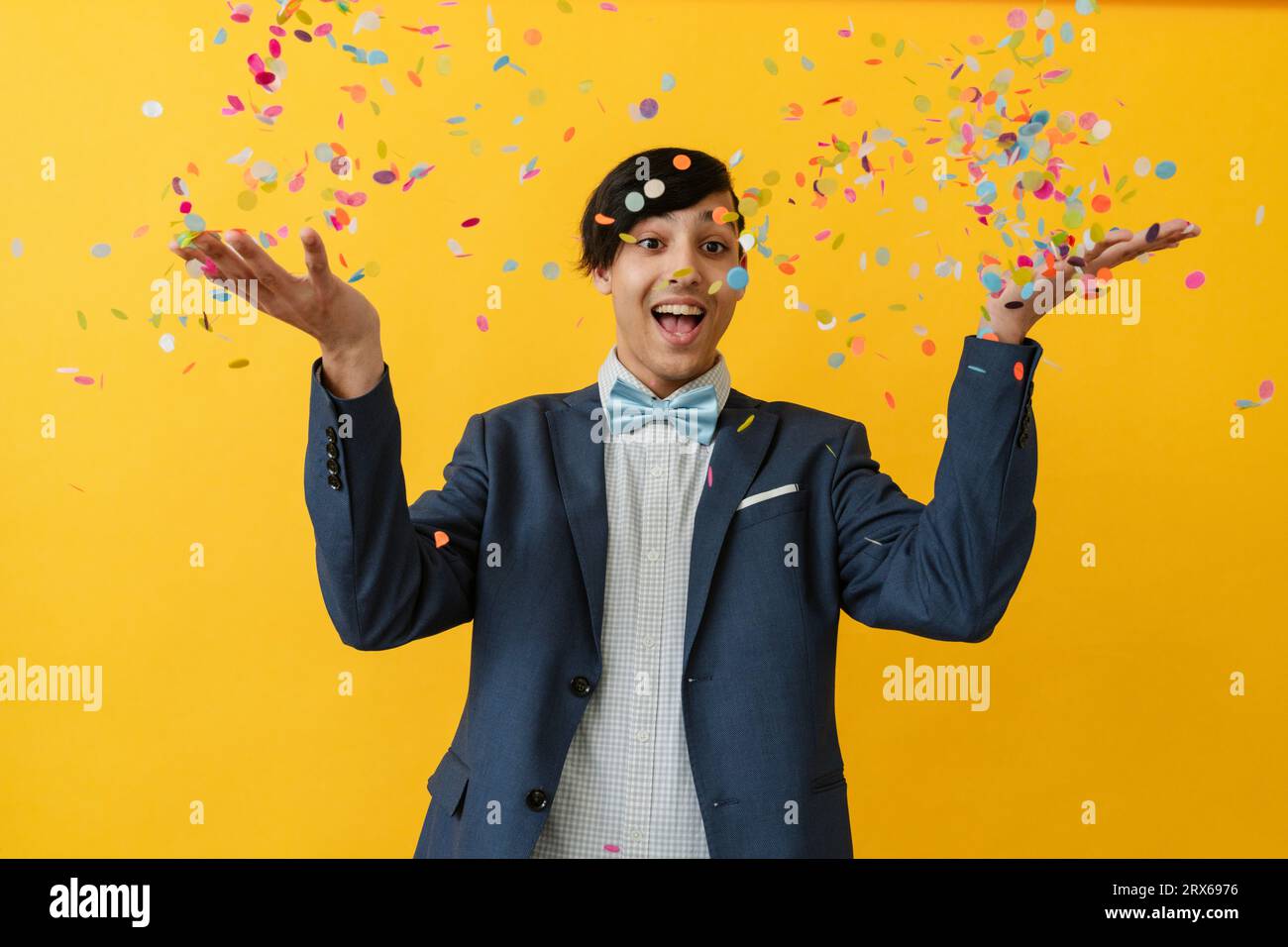 Joyful man throwing confetti and enjoying against yellow background
