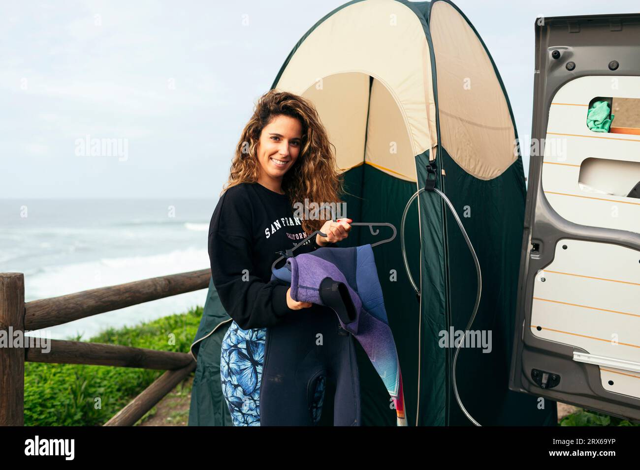 Smiling young woman with wetsuit standing outside changing tent Stock Photo