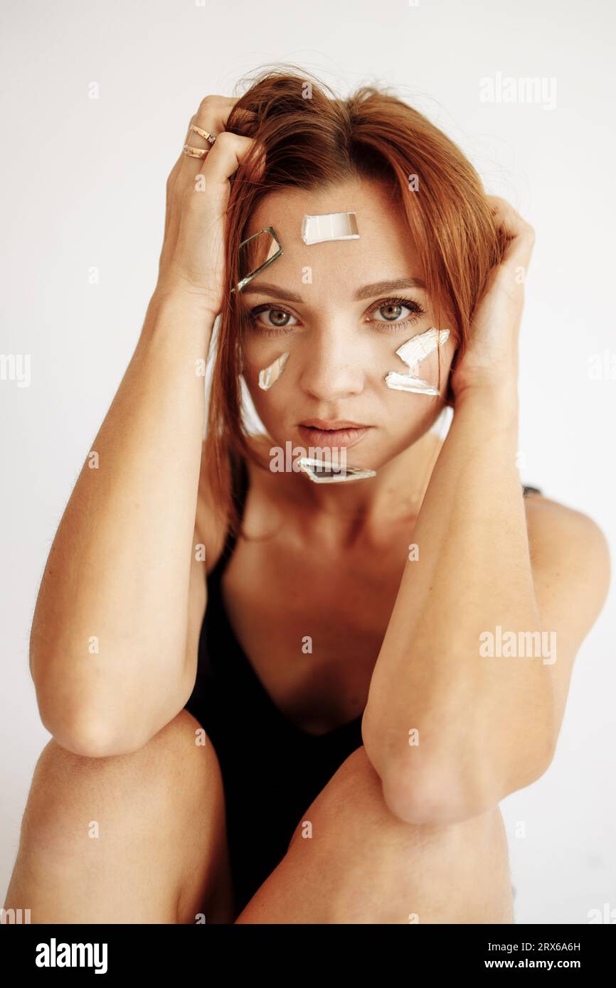 Woman with hand in hair and broken mirror pieces on face Stock Photo