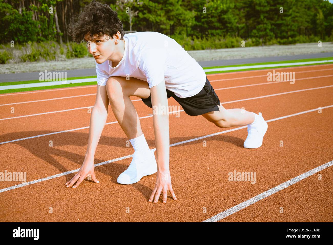 Teenage boy preparing for running race on track in stadium Stock Photo