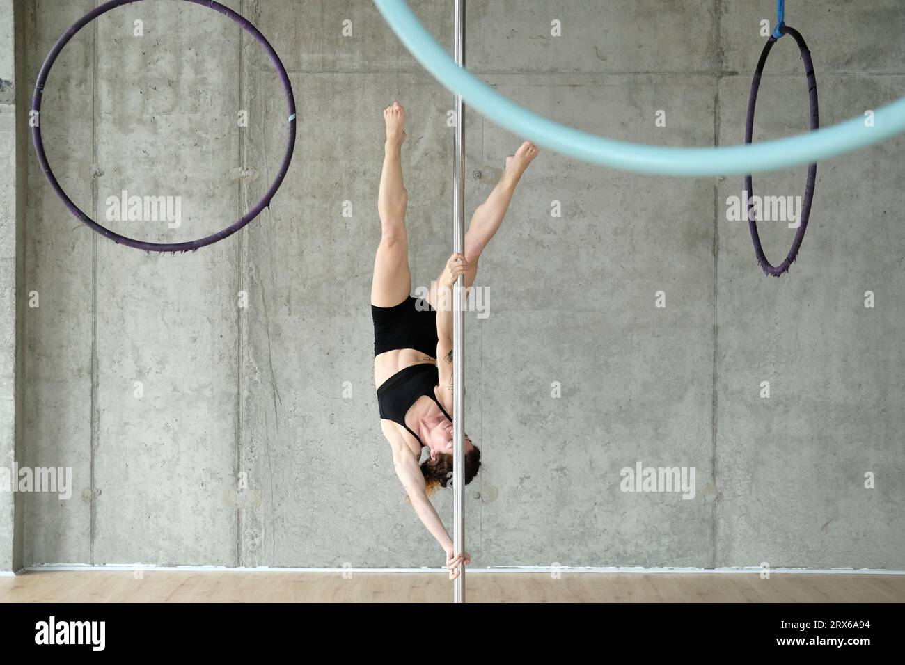 Woman practicing gymnastics on pole in front of concrete wall Stock Photo